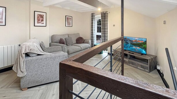 Ein Wohnzimmer mit grauem Sofa, einem Fernseher und einer Treppe.