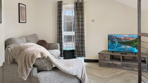 Ein modernes Wohnzimmer mit einer Couch, einem Fernseher und einem Fenster mit Vorhängen.