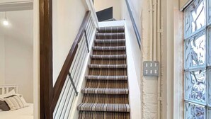 Eine Treppe mit Streifenmuster, ein Bett mit weißer Bettwäsche und eine dekorative Glasdoor.