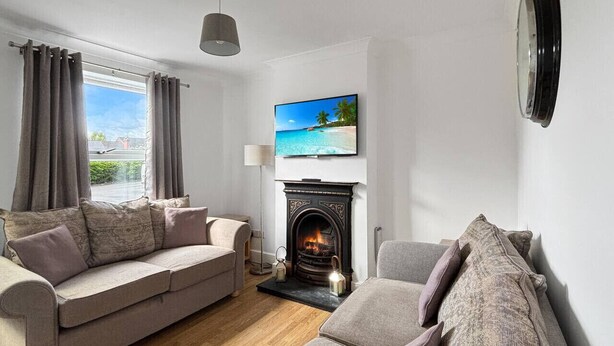 A living room with a fireplace, a sofa set, a television, and a window with curtains. - 3bed house Sleeps8 garden driveway Free Gym Access (Lincolnshire)