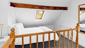 A bedroom with a wooden staircase, a bed with white bedding, a small window, and a framed picture on the wall. - 3bed house Sleeps8 garden driveway Free Gym Access (Lincolnshire)