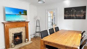 A room with a fireplace, a dining table with chairs, a television, and a cityscape painting. - 3bed house Sleeps8 garden driveway Free Gym Access (Lincolnshire)