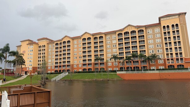 Ein mehrstöckiges Hotel mit Balkonen, einem Wasserlauf davor und einer Fußgängerbrücke.