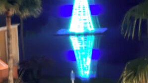 Nachtsicht auf einen Parkplatz mit einer hell beleuchteten, pyramidenförmigen Struktur.
