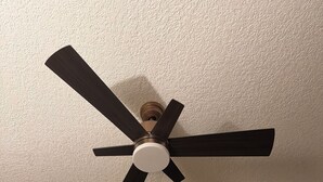 Ein Deckenventilator mit fünf Flügeln, ein an der Wand montierter Fernseher und eine Tür mit Lichtschalter.
