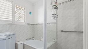 A bathroom with a bathtub, toilet, and shower area. - Bright 3-bed Retreat Near Beaches (Hervey Bay)