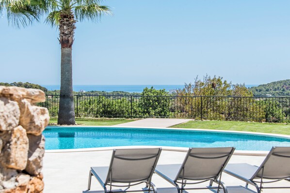 A swimming pool with lounge chairs, a palm tree, and a view of the sea. - Luxury Villa Overlooking Sea (PM)