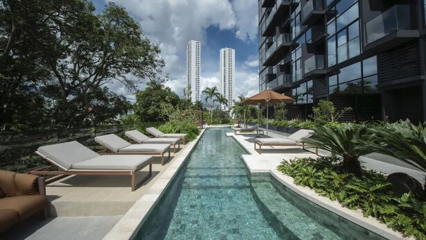 Una piscina con sillas de descanso, rodeada de follaje y edificios modernos.