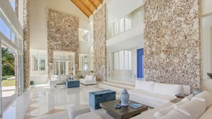 A spacious living area with a high ceiling, a stone wall, and a large window. - Stunning 6br Villa With Ocean View in Cap Cana (Punta Cana)