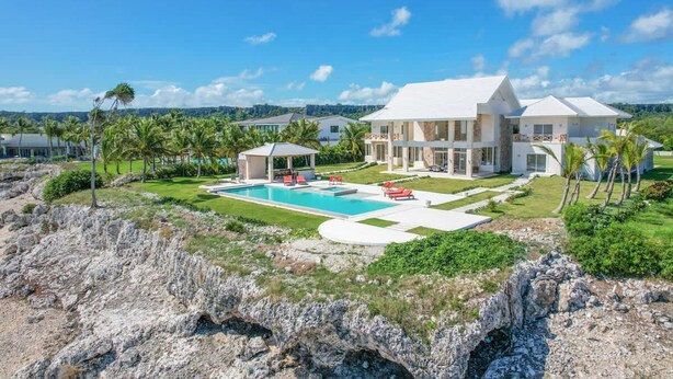 A large house with a swimming pool, surrounded by greenery and palm trees. - Stunning 6br Villa With Ocean View in Cap Cana (Punta Cana)
