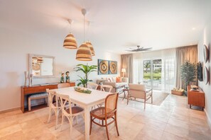 A spacious living room with a dining area, large windows, and a ceiling fan. - Apartment w Pool Ocean View at Punta Palmera Ba5 (Punta Cana)