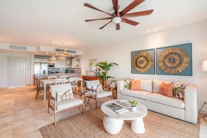 A modern living room with a white sofa, a coffee table, and a dining area with chairs and a table. - Apartment w Pool Ocean View at Punta Palmera Ba5 (Punta Cana)