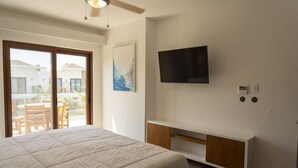 Una camera da letto con un letto, una TV a muro, una porta scorrevole su un balcone e una ventola a soffitto.
