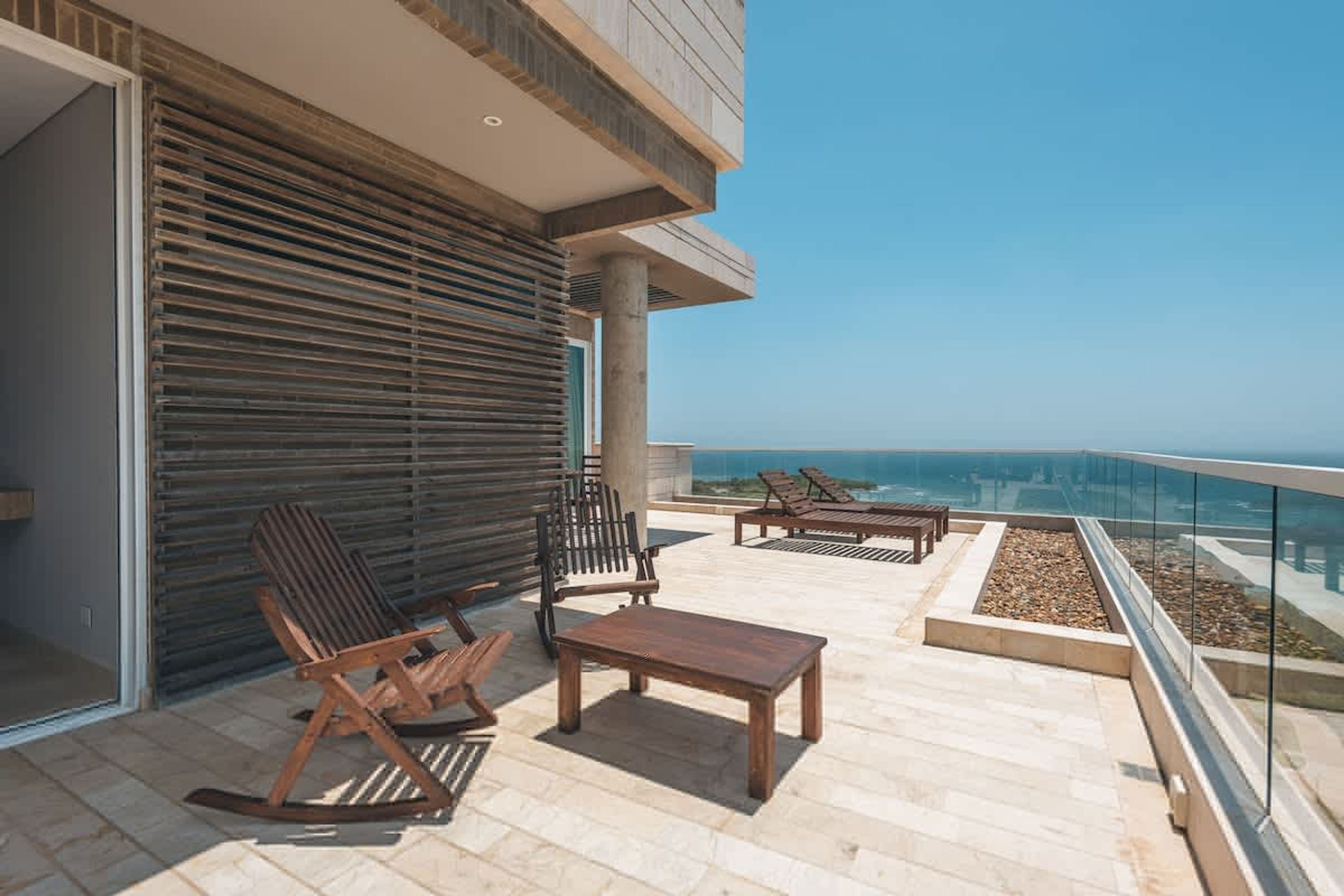 Un balcone con mobili da esterno, vista sull'oceano e facciata di un edificio moderno.