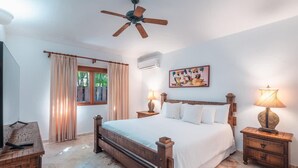 A bedroom with a wooden bed, two bedside tables with lamps, a ceiling fan, a window with curtains, and a wall-mounted air conditioner. - 3br Villa Private Pool 6 Guests in Casa de cam (La Romana)