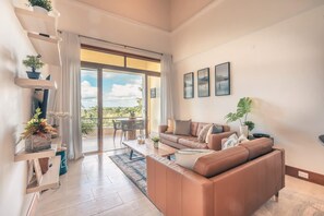 A spacious living room with a brown leather sofa, a coffee table, and a balcony with a view. - 1br 4 Guests Golf View Course Casa de Campo (La Romana)