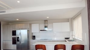 A modern kitchen with a stainless steel refrigerator, white cabinets, a built-in oven, and a central island with bar stools. - 2br 4 Guests Balcony and Pool View Cap Cana (Punta Cana)