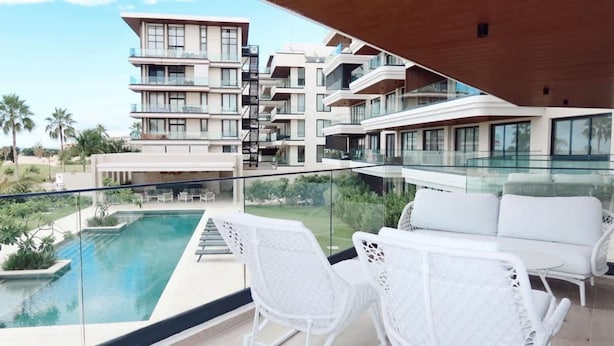 A modern hotel with a pool, white outdoor furniture, and a view of other buildings. - 2br 4 Guests Balcony and Pool View Cap Cana (Punta Cana)