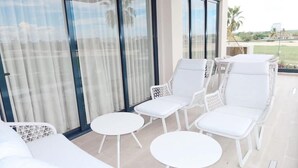 A balcony with white wicker furniture, including chairs and tables, and a view of the outdoors. - 2br 4 Guests Balcony and Pool View Cap Cana (Punta Cana)