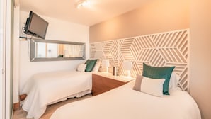 A hotel room with two beds, a TV mounted on the wall, and a geometric-patterned headboard. - Modern 2br-apartment w Golf View at Casa de Campo (La Romana)