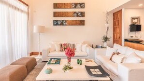 A modern living room with a white sofa, a coffee table with a vase of flowers, and three abstract paintings on the wall. - Modern 2br-apartment w Golf View at Casa de Campo (La Romana)
