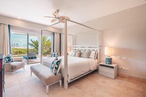 Un lit à baldaquin avec un ventilateur de plafond, une table de chevet avec une lampe, un banc et une vue sur la plage.