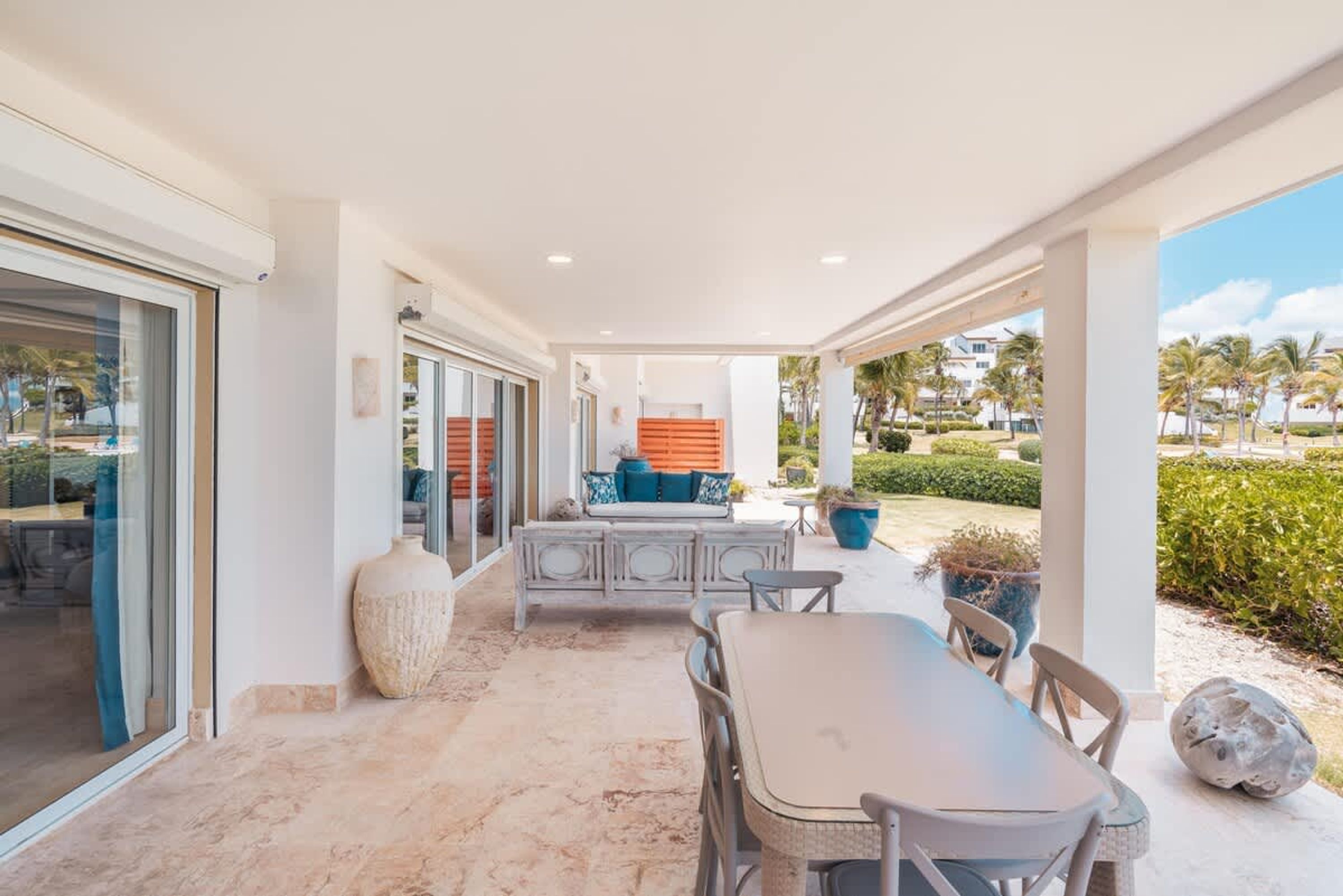 A covered outdoor patio with a dining table and chairs, a seating area with cushions, and a large vase.
