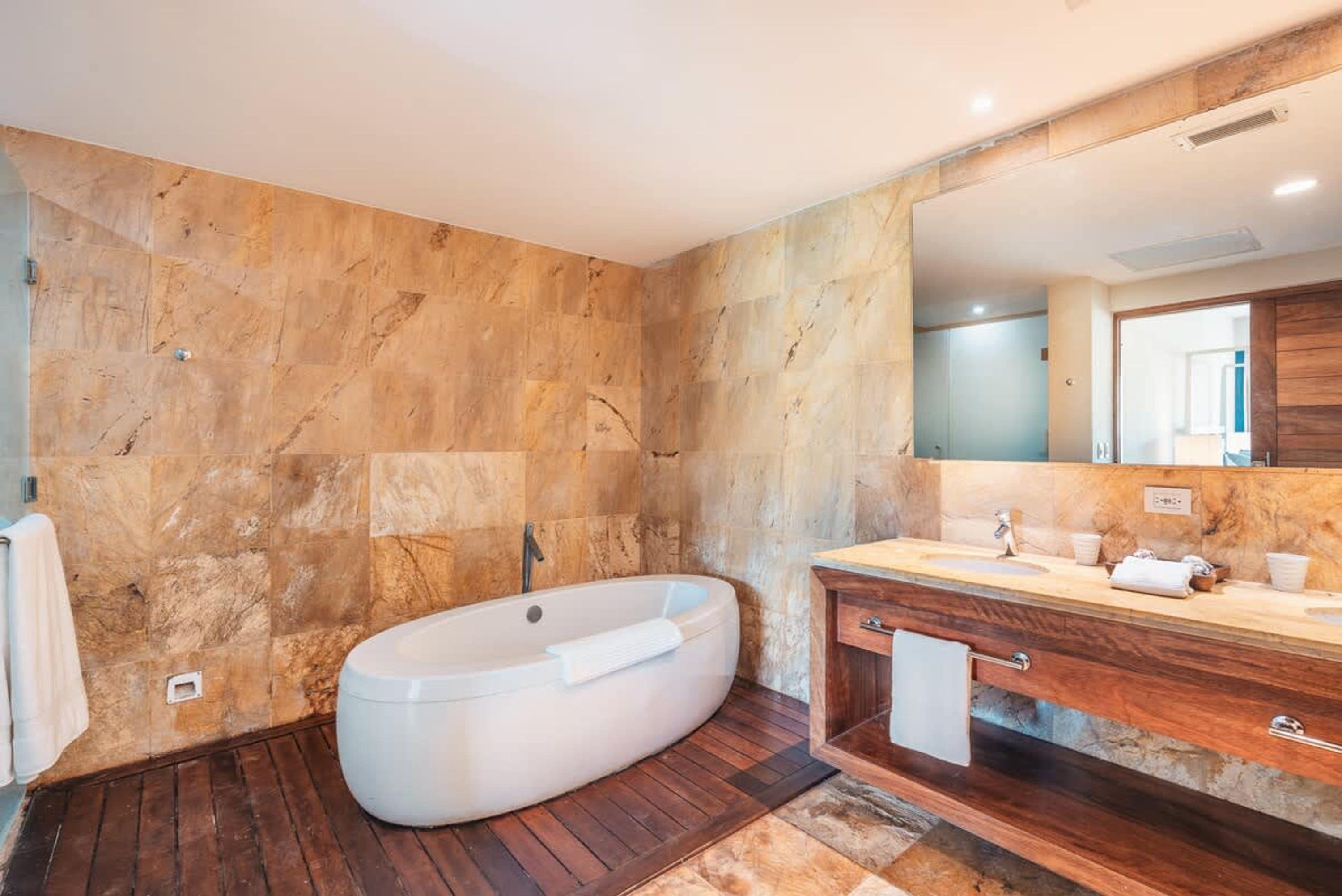 Un baño moderno con una bañera independiente, un tocador de madera y un espejo grande.