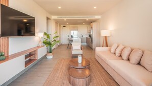 Un salon moderne avec un canapé, une table basse, un téléviseur et une cuisine en arrière-plan.