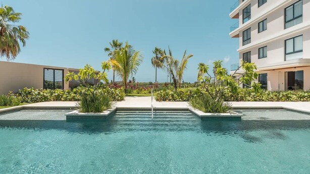Une piscine à l’eau d ’un bleu cristallin, entourée de verdure et de bâtiments modernes.