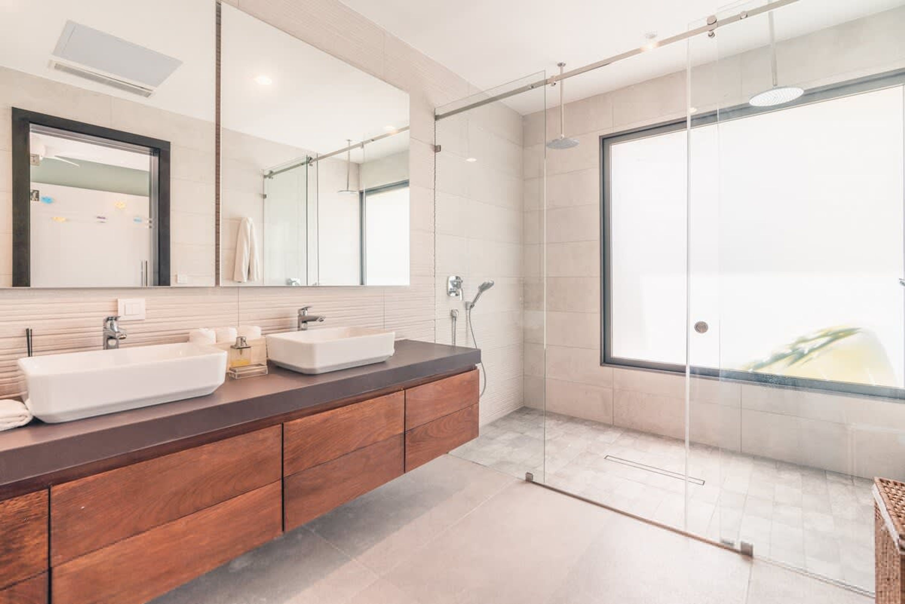 A modern bathroom with a large mirror, two sinks, a shower, and a glass door leading to a balcony.