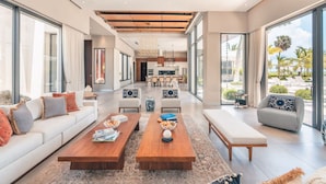A spacious living area with a sofa, coffee table, and seating, leading to a kitchen and dining area.