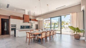 A modern kitchen with a dining area, large windows, and a view of palm trees.