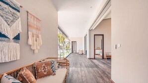 A hallway with a wooden floor, a sofa with cushions, and a wall with a woven tapestry.