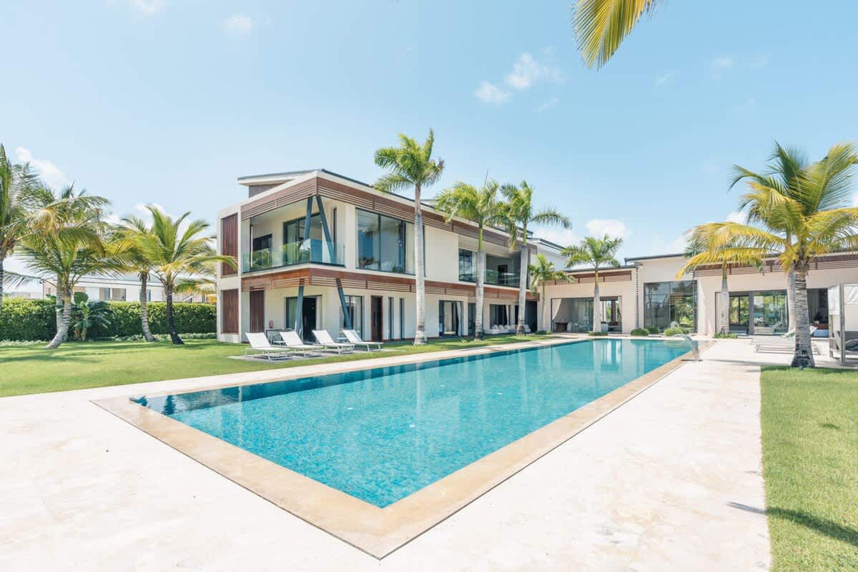 A modern two-story building with a swimming pool, palm trees, and a clear sky.