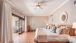 Hotellihuone, jossa on sänky, työpöytä, tuoli, kattotuuletin ja näkymä lasiovesta.