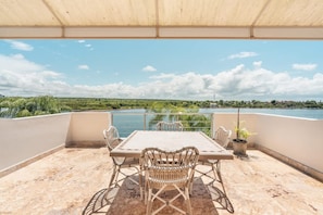 A terrace with a table and chairs, overlooking a body of water and greenery. - Prime Location 5 Bedrooms 16 Guests Casa de Campo (La Romana)