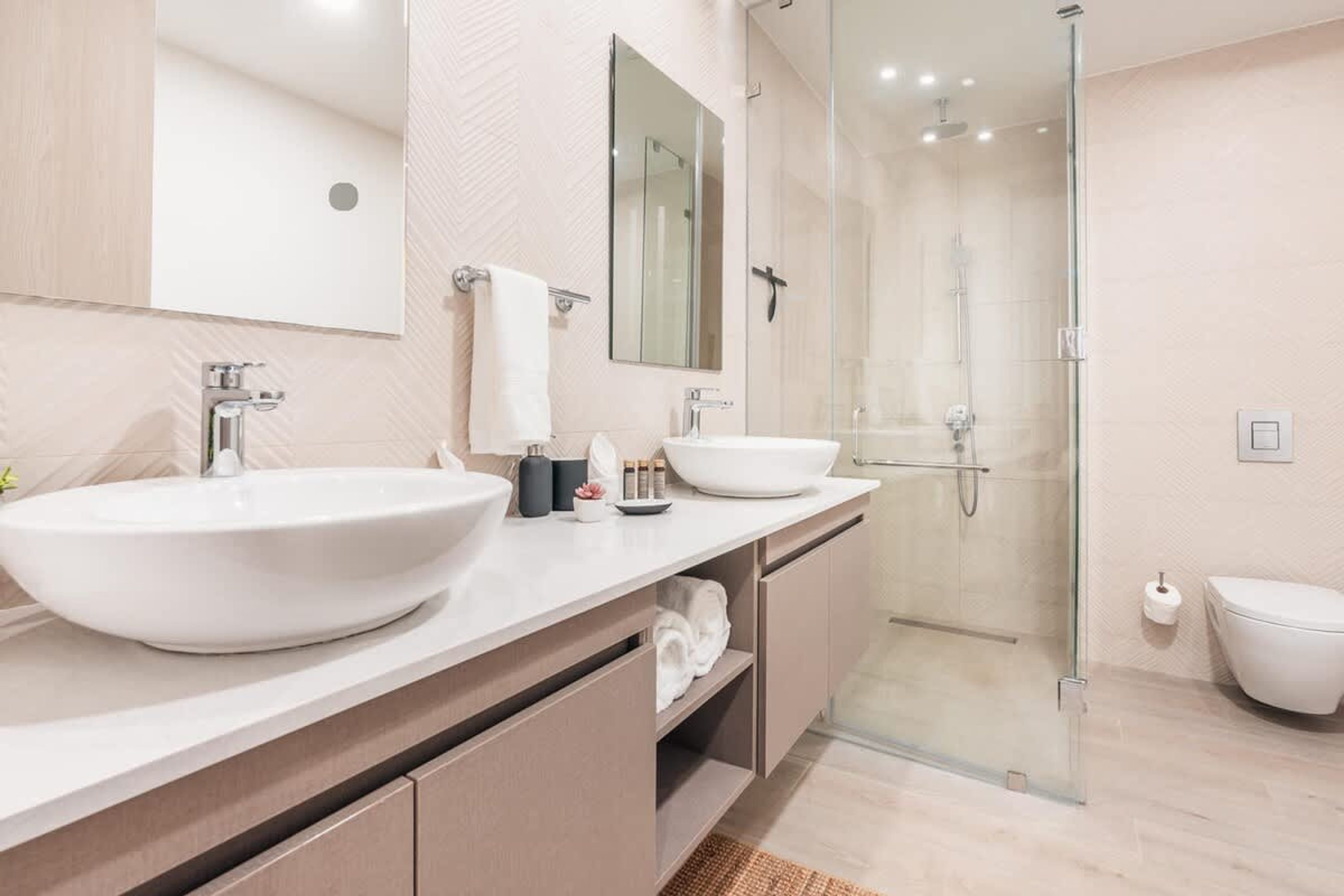 Un baño moderno con dos lavamanos grandes, una cabina de ducha de vidrio y un inodoro.