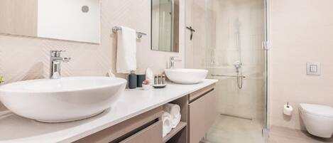 Un baño moderno con dos lavamanos grandes, una cabina de ducha de vidrio y un inodoro.