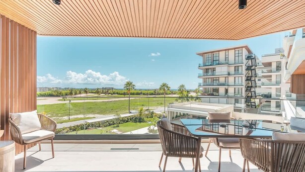 Un balcón con una mesa y sillas de vidrio, con vistas a una zona residencial y un cielo despejado.