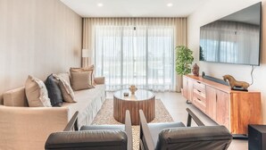 Una sala de estar moderna con sofá, mesa de centro, televisor y un ventanal con cortinas.