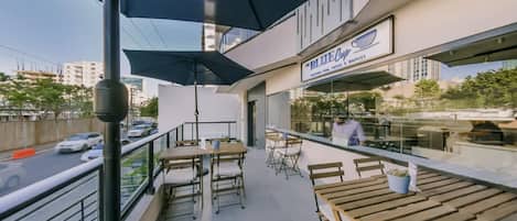 Un área de estar al aire libre con mesas y sillas, un letrero que dice 'The Blue Cup', y vistas de la calle.