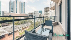 Ein Balkon mit Korbmöbeln, einem Glastisch und Blick auf Stadtgebäude.