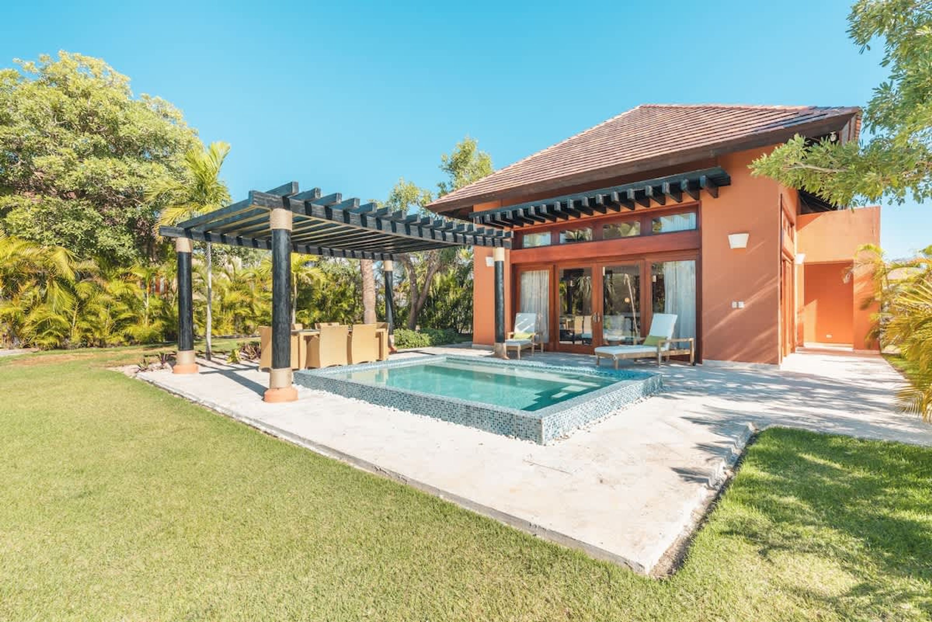 A modern house with a swimming pool, covered patio, and lush greenery.