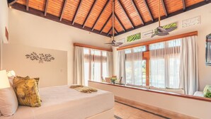 Une chambre d’hôtel avec un lit, un ventilateur de plafond, de grandes fenêtres avec des rideaux et un plafond en bois.
