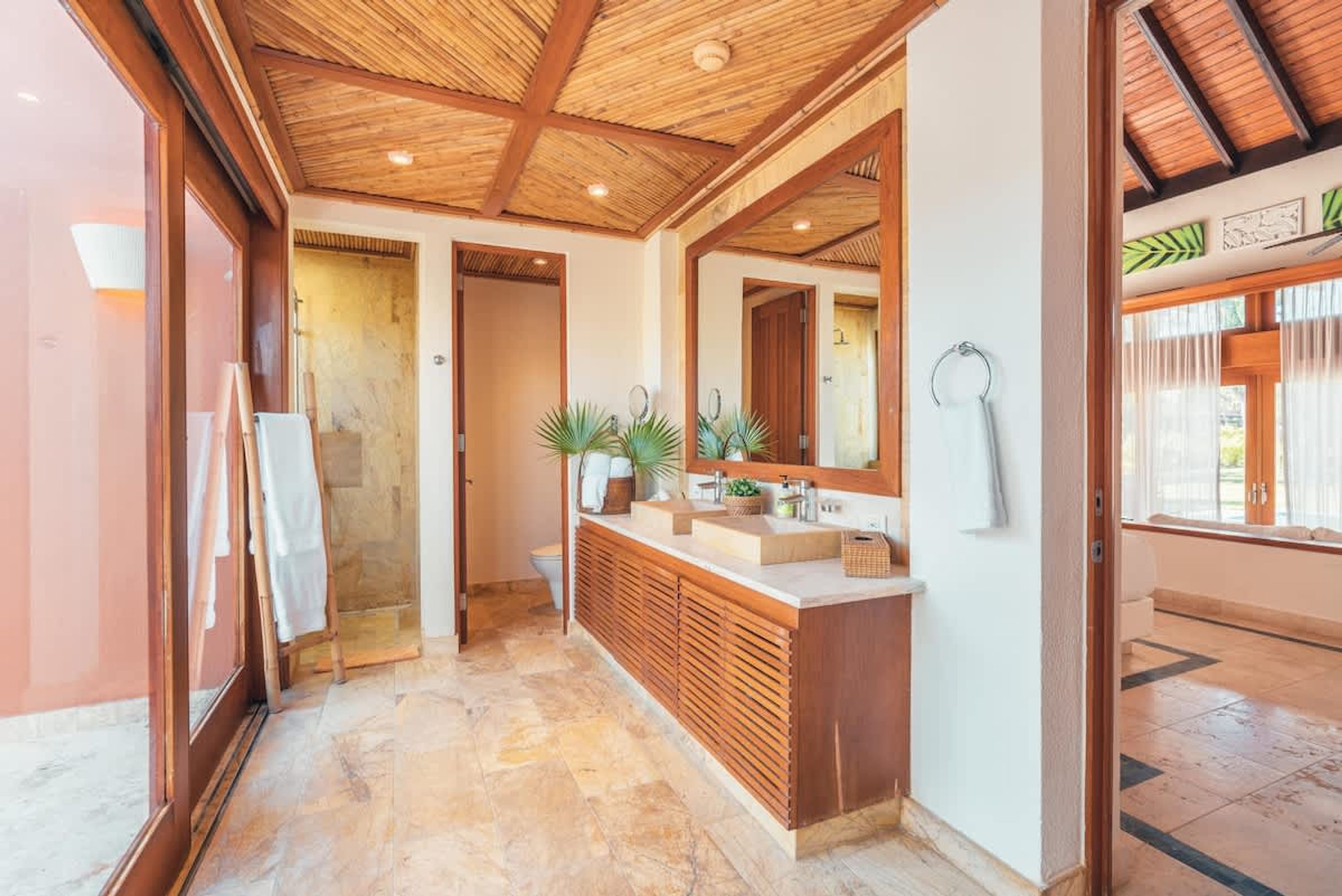 A bathroom with a wooden ceiling, a large mirror, a sink, and a shower area.