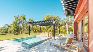 Une piscine agrémentée d’une pergola, de chaises longues et offrant une vue sur la végétation environnante.