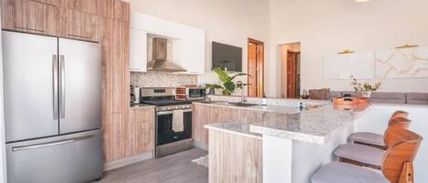 Una cocina moderna con armarios de madera, electrodomésticos de acero inoxidable, una isla central con taburetes de bar y un techo alto con vigas a la vista.
