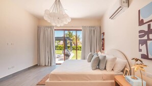 A bedroom with a large bed, a wooden floor, a ceiling light, and a view of the outdoors.