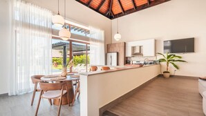 A modern kitchen with a central island, wooden flooring, and a dining area with chairs and a table.